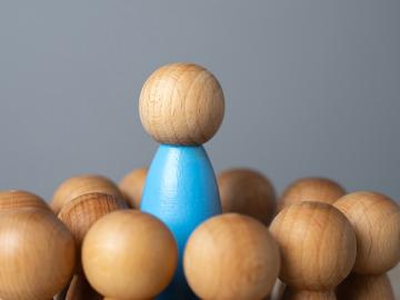 Wooden people are placed in a circle around one wooden person standing above the circle