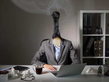 a woman seated at a desk with her head replaced by a burned matchstick