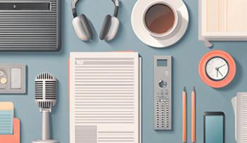 An aerial view of a blue desk with keyboard, headphones, coffee, notes, microphone, and more on the table.